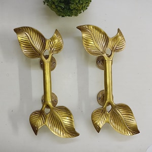 May include: Two gold leaf-shaped door handles with a decorative design. The handles are made of metal and have a polished finish.