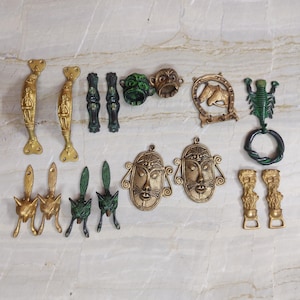 May include: A collection of assorted metal hardware including two long gold-toned handles, two dark green vertical pulls, two small round face ornaments, a horseshoe with horse heads, a green scorpion ring, four fox-shaped pulls, two oval masks, and two small figures.