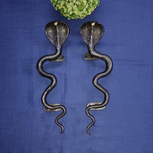 May include: A pair of black metal door handles shaped like cobras with detailed carvings. The handles are mounted on a blue surface.
