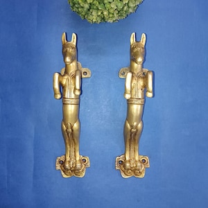 May include: A pair of gold-toned metal door handles shaped like standing horses. The handles have intricate details and a decorative base.