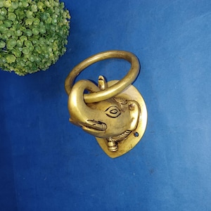 May include: A gold-colored metal elephant head door knocker with a ring handle. The elephant's trunk is curled around the ring.