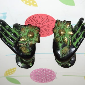 May include: A pair of black and green metal door handles shaped like hands with a flower design. The handles are ornate and have a traditional Indian style.