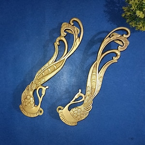May include: Two ornate gold-toned metal door handles shaped like peacocks with intricate details. The handles are on a blue background.