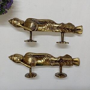 May include: Two gold-toned door handles shaped like reclining Buddha figures. Each handle has a detailed design and a base for mounting.