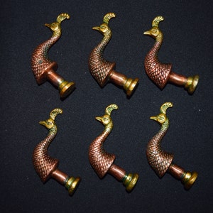 May include: Six peacock-shaped drawer pulls in a copper and gold finish. The pulls are made of metal and have a detailed design.