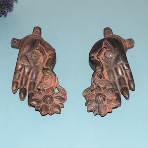 Puede incluir: Dos manos ornamentadas de metal marrón oscuro sosteniendo una flor, cada una con detalles intrincados y un acabado ligeramente desgastado.