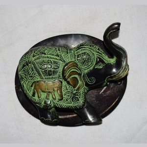May include: A green and black metal elephant door knocker with intricate details. The elephant is standing on a round wooden base.