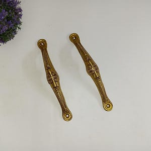 May include: Two ornate gold-toned metal drawer pulls with intricate designs.