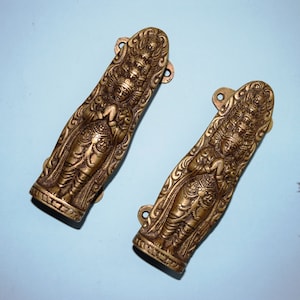 May include: A pair of ornate brass door handles with intricate carvings of a deity. The handles are in a warm gold tone and have a traditional design.