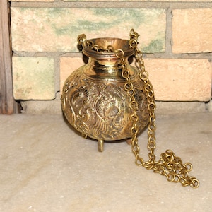 May include: A vintage brass incense burner with detailed floral patterns and three small feet. The burner features a decorative chain and a round body. The brass has a warm, golden colour, and the design suggests a historical or cultural significance.