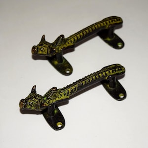 Puede incluir: Dos manijas de puerta antiguas de latón con diseño de dragón. Las manijas son de color verde oscuro y negro con detalles intrincados, incluida una cabeza de dragón en cada extremo. Montadas sobre una base negra con orificios para tornillos.