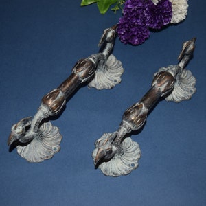 May include: Two antique brass door handles with a peacock design. The handles are in a distressed finish with a white patina.