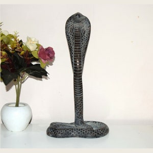 May include: A black metal sculpture of a cobra with its hood raised. The sculpture is detailed with scales and has a textured finish.