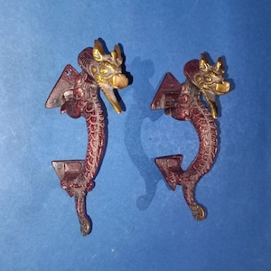 Peut inclure: Deux poignées de porte en laiton ornées en forme de dragons avec des accents dorés. Les poignées sont de couleur rouge foncé et présentent des détails complexes.