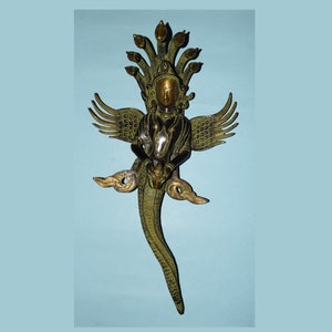 May include: A green and gold metal sculpture of a deity with multiple snake heads and wings. The deity is holding a small object in its hands.