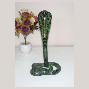 May include: A green and black cobra statue with a gold-colored head. The statue is made of metal and has a detailed design.