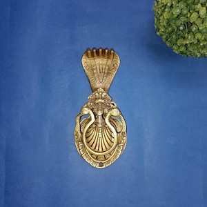 Può includere: Un batacchio per porta dorato con un designo dettagliato di un cobra e due pavoni. Il batacchio è di forma ovale e ha un anello per bussare.