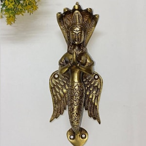 Pode incluir: Puxador de porta de latão com uma figura com capuz de cobra, mãos em oração e cauda de sereia. A maçaneta tem asas detalhadas e uma base decorativa, ideal para adicionar um toque único a qualquer porta. A maçaneta tem aproximadamente 20 cm de altura.