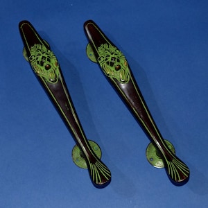 Puede incluir: Dos manijas de puerta antiguas con acabado marrón oscuro y detalles de cabeza de león verde. Las manijas tienen una forma larga y delgada con detalles verdes decorativos y placas de montaje circulares. Las manijas son de metal.