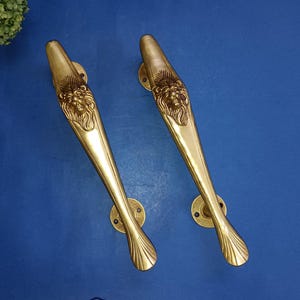 May include: A pair of ornate brass door handles with lion head designs. The handles are long and slender with a decorative, fan-shaped end.