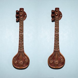 Puede incluir: Dos tiradores de puerta de latón adornados con forma de instrumentos sitar. Los tiradores son de color marrón oscuro con detalles intrincados.