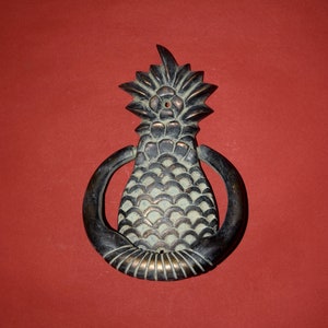 May include: A bronze pineapple door knocker with a ring handle. The pineapple is detailed with scales and a crown.