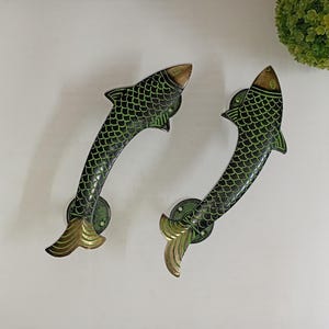 Könnte beinhalten: Zwei grün-schwarze, fischförmige Türklinken mit goldenen Akzenten. Die Griffe sind aus Messing und haben ein detailliertes Design.