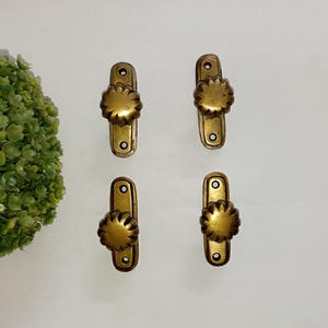 Könnte beinhalten: Vier antike Messing-Schrankknöpfe mit einem dekorativen, geriffelten, runden Design. Jeder Knopf ist an einer rechteckigen Platte mit zwei Löchern zur Montage befestigt.