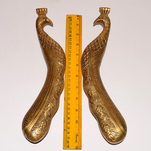 Puede incluir: Un par de tiradores de puerta en forma de pavo real de color dorado. Los tiradores miden aproximadamente 30 cm de largo y presentan detalles intrincados.