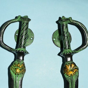 May include: A pair of decorative door handles shaped like swords. The handles are made of metal and have a green and gold finish.