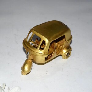 May include: A gold-colored miniature auto rickshaw, a three-wheeled vehicle. The model has detailed features, including a driver's seat and wheels. The vehicle is made of a shiny, metallic material.