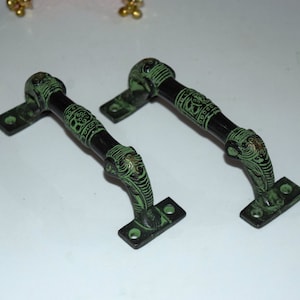 Puede incluir: Dos tiradores de puerta de metal verde con diseños intrincados. Los tiradores tienen forma de cabeza de elefante y tienen un acabado negro.