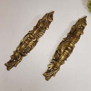 Op de afbeelding: Twee sierlijke messing deurgrepen met ingewikkelde bloemmotieven. De grepen zijn goudkleurig en hebben een decoratief, rolvormig ontwerp.