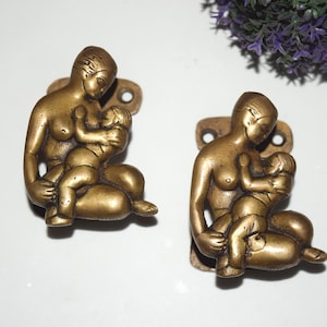 May include: Two antique brass door handles, each depicting a mother holding a child. The handles are detailed and have a vintage look.