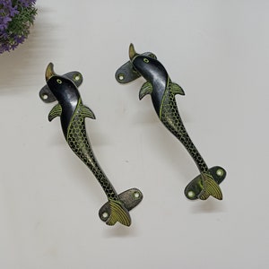 Könnte beinhalten: Zwei schwarze und grüne Delfin-Türgriffe mit Messing-Finish. Die Griffe sind mit einer detaillierten Delfin-Form gestaltet und haben ein grünes und schwarzes Muster.