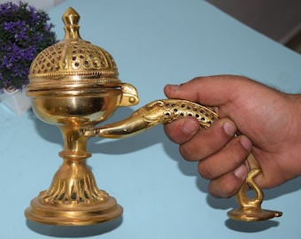 May include: A gold metal incense burner with a decorative handle shaped like a bird. The burner has a round top with a perforated lid and a base with intricate details.