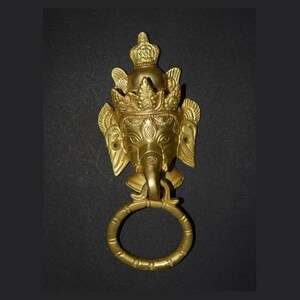 May include: A gold-coloured door knocker shaped like the head of an elephant with a crown on its head. The knocker has a ring attached to its trunk.