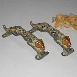 May include: A pair of antique brass door handles shaped like tigers. The handles are detailed with tiger stripes and have a gold finish.