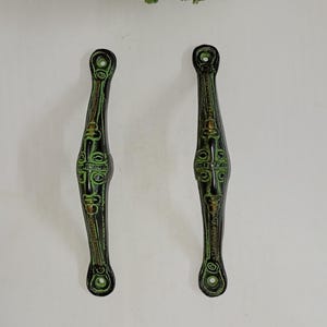 Könnte beinhalten: Ein Paar antike Türgriffe mit grüner und goldener Oberfläche. Die Griffe sind aus Metall und haben ein dekoratives Design.
