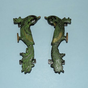 Może przedstawiać: Para ozdobnych, zielonych i złotych klamki do drzwi w kształcie pawia. Klamki są wykonane z metalu i mają szczegółowy wzór.