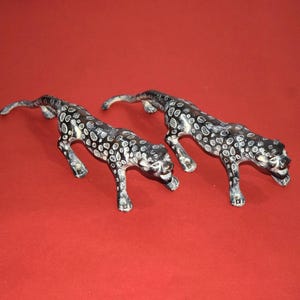 May include: Two decorative leopard figurines. The figurines are black with white spots and are posed in a stalking position. The background is a solid red color.