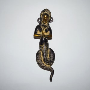 Könnte beinhalten: Ein goldener und schwarzer Türknauf in Form einer Frau mit einem Schlangen Schwanz. Die Frau ist in einer Gebetsposition mit ineinander verschränkten Händen.