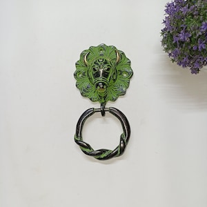 May include: Green and black metal door knocker with a bull's head design. The knocker has a twisted rope-like ring.