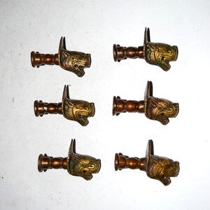 May include: Six bronze-colored curtain rod finials with a detailed dragon head design. The finials have a cylindrical body and a decorative dragon head with intricate detailing. The dragon heads are a mix of bronze and gold tones.