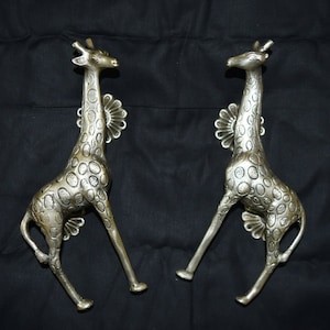 Puede incluir: Un par de tiradores de puerta de jirafa plateados con un patrón de manchas detallado. Los tiradores están en posición de pie con el cuello arqueado.
