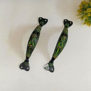 Può includere: Due maniglie decorative per porte con finitura nera e verde. Le maniglie presentano un design ornato con una figura centrale e accenti decorativi. Le maniglie sono in metallo e hanno un aspetto artistico unico.