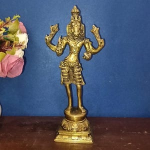 May include: A gold-colored brass statue of a deity with a horse-like head, standing on a decorative base. The figure has multiple arms and is adorned with intricate details. The statue is set against a blue background.