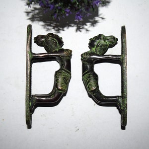May include: A pair of antique brass door handles in the shape of women. The handles are green with a patina finish.