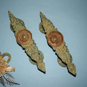 May include: Two ornate door handles with a green and gold finish. The handles have a floral design and a large, round, gold center.