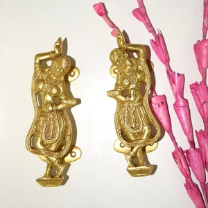 Può includere: Due maniglie per porte in metallo dorato a forma di figure danzanti. Le figure sono riccamente dettagliate e hanno un design tradizionale indiano.